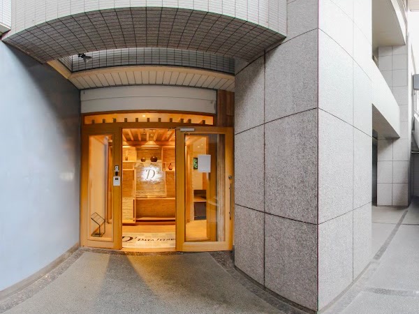 地下の中庭に面した、淡い木枠のガラス扉の入口。扉越しに光る「Df」のロゴ、右に御影石の柱。