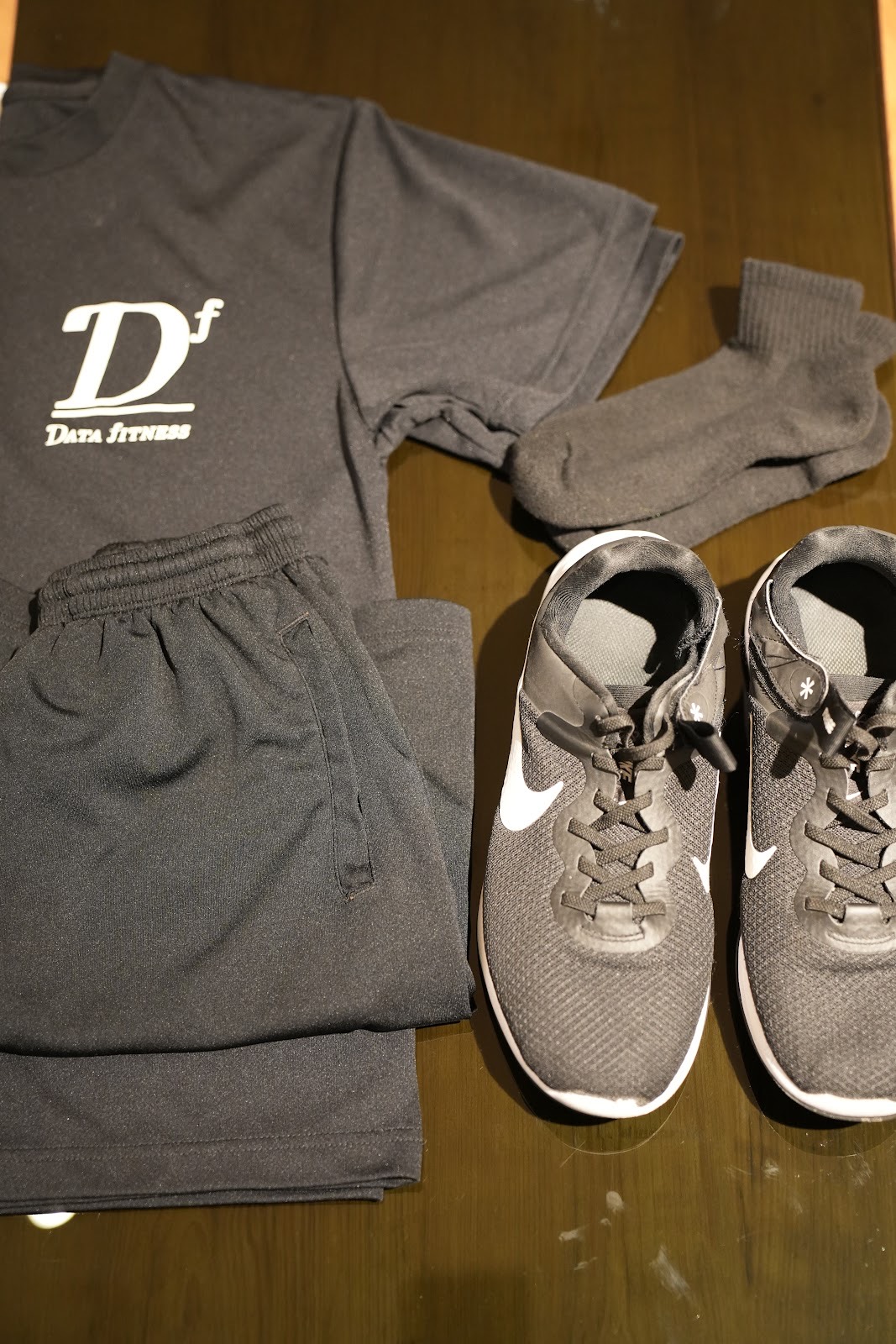 木のベンチに並べたダークグレーのレンタルウェア一式。Dfのロゴ入りTシャツ、ショートパンツ、靴下、ランニングシューズ。