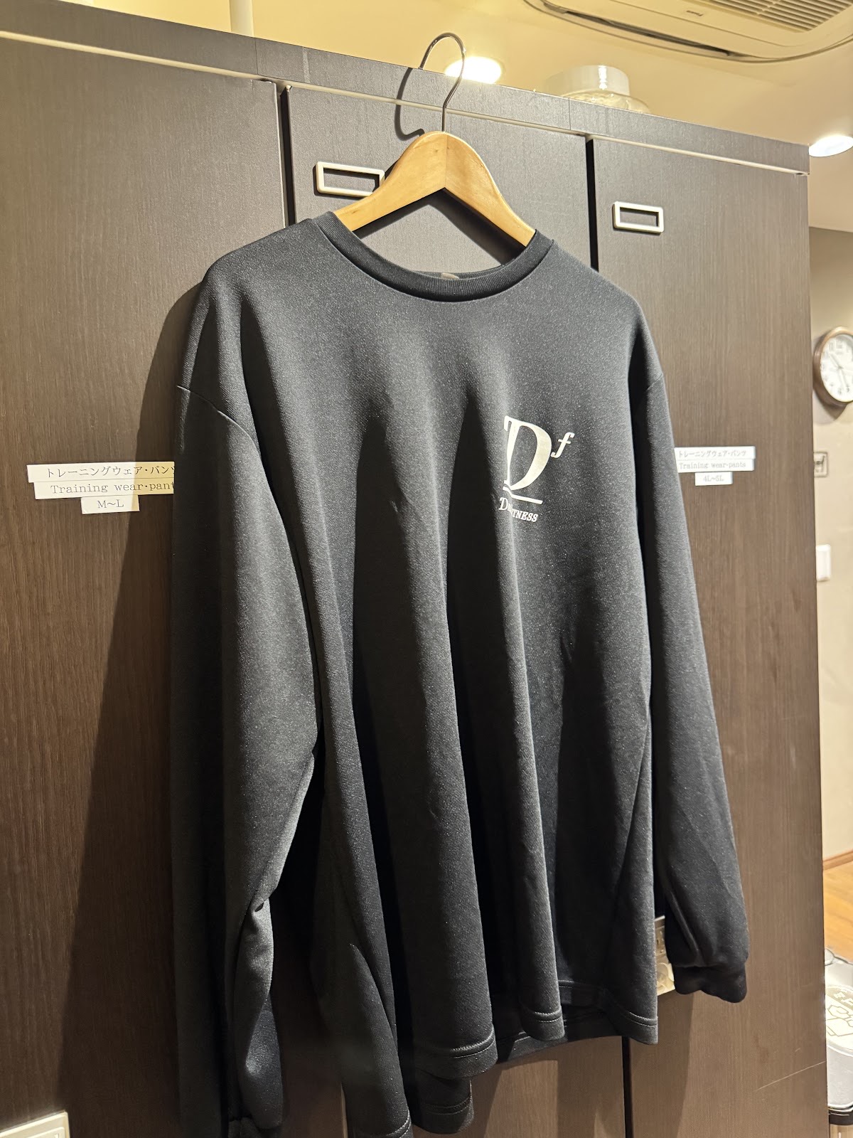 黒いロッカーの前、木のハンガーに掛けた小さなDfロゴ入りの黒い長袖ウェア。